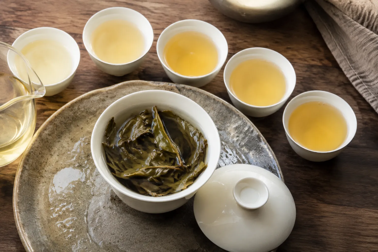 Wet white tea cake leaves opening across several infusions with pale cups nearby